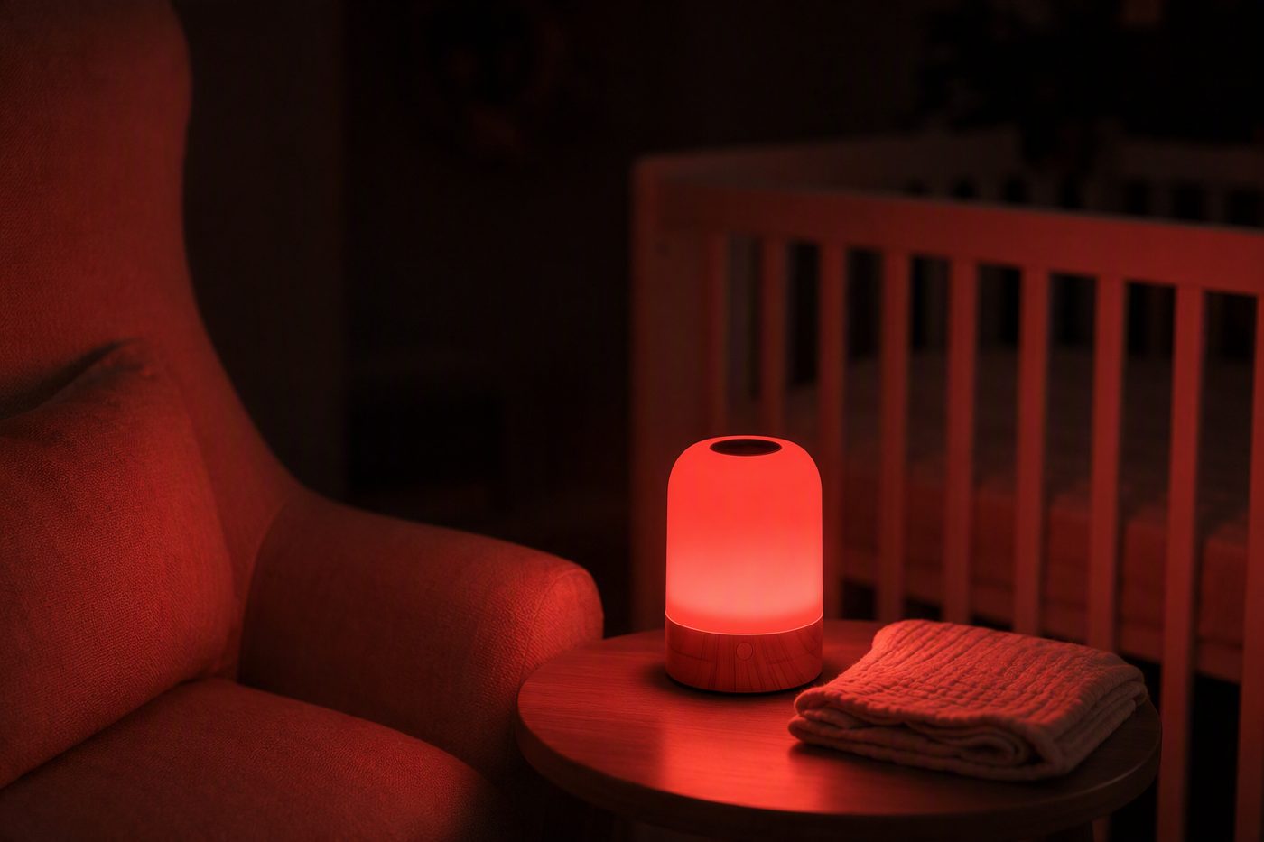 A red bedside lamp glowing on a side table next to an empty nursing chair, with a cot in the background.